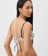Top de bikini de microfibra color blanco con estampado de caracolas, caracoles y estrellas de mar negras. Cuenta con diseño de media copa, aro estructurado y breteles regulables con detalles metálicos.