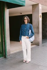 Chaqueta de denim azul con cuello redondo, manga larga y cierre frontal con botones dorados. Presenta costuras verticales decorativas y puños con botones a juego.