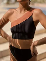 Top de bikini de un solo hombro con diseño bicolor, combinando negro y tostado. Está confeccionado en tejido de punto de alta calidad con propiedades de secado rápido y protección.