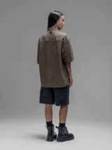 Camisa de manga corta color verde militar, con cuello clásico y cierre de botones frontales. Presenta un estampado floral en relieve.