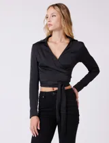 Blusa negra de satén, marca Allie Rose, con cuello con solapa y escote en V. Diseño cruzado con lazo de ajuste lateral y manga larga con pretina, ojal y botón.