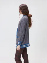 Cardigan de punto trenzado en color negro con detalles en color crema en los bolsillos, puños y ruedo. Presenta un diseño oversize, cierre frontal con botones y bordado decorativo en uno de los bolsillos delanteros.