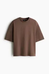Remera de algodón pesado color marrón, de corte oversized con hombros caídos, cuello redondo ribeteado y mangas cortas holgadas.