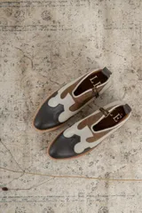 Botinetas estilo western de caña baja, confeccionadas en una combinación de cuero liso y gamuza en tonos marrón oscuro, marrón medio y crema. Presentan cierre lateral, taco bajo cuadrado y diseño con recortes característicos del estilo cowboy.