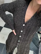 Vestido midi de punto color negro con detalles dorados, escote en V, mangas largas y abertura frontal.