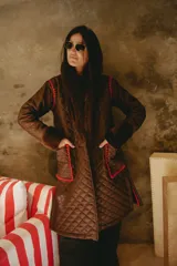Campera larga acolchada color marrón, con diseño matelassé, detalles de piel sintética en el cuello y puños, y bordados artesanales en crochet color rojo en los bolsillos y costuras.