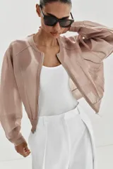 Chaqueta estilo bomber de punto color beige con acabado brillante, cuello redondo, manga larga con puños elásticos y cierre frontal con cremallera.