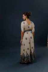 Vestido largo beige con estampado paisley en color azul marino, escote en V profundo con detalle bordado, mangas cortas amplias, cordón ajustable en la cintura con borlas y volados en el ruedo.