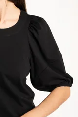 Remera de algodón negro con mangas cortas abullonadas, cuello redondo y costura central frontal.
