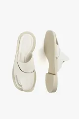 Sandalias planas de cuero color blanco hueso, con dos tiras anchas cruzadas en la parte superior y diseño minimalista.