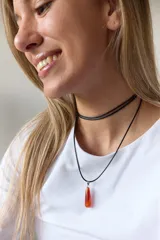 Gargantilla de cuero negro con dije de piedra blanca en forma de lágrima con engarce dorado.