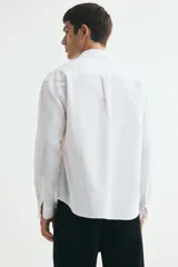 Camisa H&M de corte relajado, confeccionada en tejido liviano de mezcla de lino y algodón color blanco. Presenta cuello inglés, cierre frontal de botones, manga larga con puños ajustables y bolsillo aplicado en el pecho.