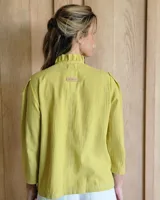 Camisa de manga tres cuartos color beige con cuello con volados y botones frontales. Presenta un detalle de color negro en la parte superior de las mangas.