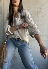 Camisa beige de manga larga con cuello en V, cierre frontal de botones y delicados bordados florales en marrón en la zona del pecho y en los puños.