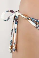 Calzón de bikini con tiras laterales ajustables y diseño estampado con patrón paisley en tonos azules, marrones y naranjas sobre fondo blanco. Cuenta con apliques metálicos decorativos en los cordones.