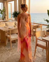 Vestido largo de satén con estampado degradado en tonos rosado, naranja y fucsia. Presenta escote en V, tirantes finos y un pañuelo integrado al cuello.