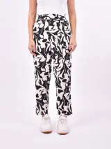 Pantalón babucha de tiro alto con cintura fruncida y lazo para ajustar. Estampado de hojas tropicales en tonos naranja y marrón sobre fondo blanco.