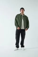 Campera verde militar de canvas de algodón grueso, con cuello clásico, cierre frontal con botones a presión, bolsillos con cierre en el pecho y corte holgado.