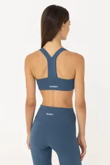 Top deportivo azul con espalda abierta y breteles finos. Tiene sujeción media y banda inferior en la cintura. Cuenta con forrería suave y liviana con abertura para colocar tazas.