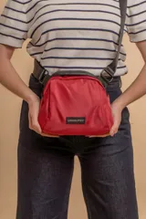 Bandolera de diseño compacto confeccionada en tafeta liviana color rojo. Cuenta con cierre superior, correa ajustable ancha y etiqueta frontal con el logo de la marca Lincoln's.