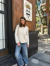 Cárdigan de lana color crudo, de tejido fino, con cuello redondo y cierre frontal de botones.