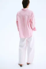 Camisa oversized a rayas color rosado y blanco, con cuello clásico, cierre frontal de botones, un bolsillo aplicado en el pecho y mangas largas con puños abotonados.