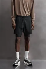 Short de entrenamiento deportivo con diseño 2 en 1, que incluye una capa exterior de tejido técnico ligero y una malla interior ajustada. Cuenta con cintura elástica con cordón de ajuste, bolsillos laterales con cierre y aberturas en el bajo.