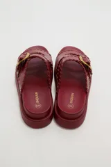 Sandalias planas de eco cuero color bordó, con tiras cruzadas y hebilla metálica dorada.