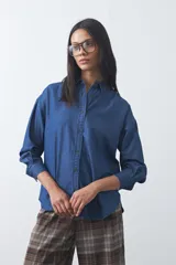 Camisa de jean en tencel con silueta amplia, hombros caídos, cuello clásico y cierre frontal con botones. Presenta ruedo curvo con tajos laterales y pliegue en la espalda.