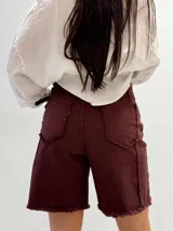 Bermuda color borgoña de gabardina elastizada, corte a la rodilla, con cinto fino con tachas y detalles de flecos en el ruedo.