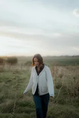 Saco tipo cardigan de punto color blanco con detalles de pespuntes decorativos en color negro a lo largo de los bordes y costuras. Presenta cuello en V, cierre frontal con botones y mangas largas.