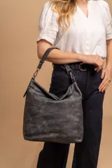 Cartera tipo bandolera de gran tamaño, confeccionada en cuero sintético con acabado desgastado. Cuenta con una asa corta fija, una correa larga regulable y extraíble, y una placa metálica con la marca en la parte frontal.