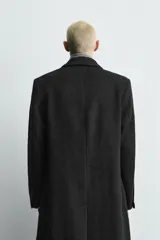 Abrigo de corte relajado confeccionado en tejido con lana, de color negro. Presenta cuello con solapas de pico, manga larga, cierre frontal de botonadura cruzada y bolsillos con solapa en la cadera.