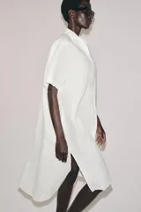 Vestido camisero de lino con cuello solapa, manga corta y cierre frontal con botones. Presenta un diseño con bajo redondeado y aberturas laterales.