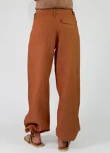 Pantalón de lino color beige, de corte holgado tipo jogger con puños ajustables con cintas en los tobillos, bolsillos laterales y cierre frontal con botón y cremallera.