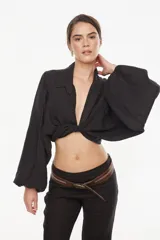 Top corto de lino italiano con diseño a cuadros en tonos verde oliva, beige y rosado, cuello camisero, mangas largas abullonadas con puños elásticos y nudo frontal ajustable.