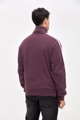 Buzo de felpa con friza, color bordó, con cuello alto y medio cierre metálico frontal. Presenta mangas largas con franjas laterales en color crema y bordado de la marca en el pecho.