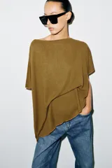 Top tipo capa blanco de punto fluido, con mezcla de viscosa, cuello bote, mangas cortas y bajo asimétrico.