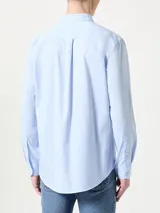 Camisa celeste de popelina de algodón flexible, con cuello abotonado, cierre con botones, puños con botones y logo de Tommy Hilfiger bordado en el pecho.