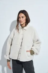 Campera de corderito color beige, con cuello camisero y cierre frontal de botones a presión. Presenta una cartera central lisa en contraste y mangas largas con puños elásticos.
