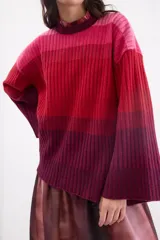 Sweater de punto con diseño en degradé de tonos fucsia, rosado y bordó. Presenta cuello a la base, corte recto holgado y mangas largas amplias con tajos en los puños.