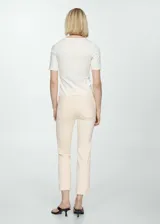Jeans estilo flare color beige, confeccionados en tejido elástico de algodón. Presentan diseño crop, tiro alto, cinco bolsillos, trabillas para cinturón y cierre frontal con cremallera y botón. Los dobladillos tienen terminación deshilachada.