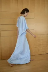 Vestido midi de tejido satinado color celeste, con cuello barco y diseño asimétrico con mangas tipo capa. Presenta un detalle drapeado en la cintura y abertura en la espalda.