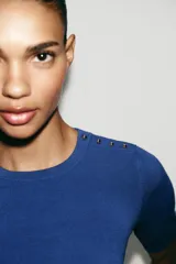 Jersey negro de punto de manga corta y cuello redondo, con detalle de botones dorados en el hombro.