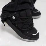 Zapatillas negras de estilo skate, con cordones gruesos y detalles en los costados.