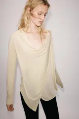 Chaqueta de punto fino color beige, con escote fluido y drapeado, manga larga y cierre frontal cruzado.