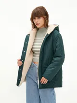 Campera acolchada de color verde oscuro con diseño matelasseado, interior forrado en corderito sintético color beige, con capucha y cierre frontal de botones a presión.