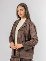 Chaqueta de estilo boho confeccionada en ecocuero agamuzado, con diseño de flecos en el frente, cierre frontal con botones y bolsillos laterales. Presenta un corte holgado y forro interior.