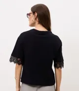 Remera de algodón blanca de corte recto, con cuello redondo, mangas cortas amplias y detalle de encaje aplicado en los puños.
