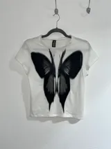 Remera corta negra de algodón con estampado de mariposa blanca.